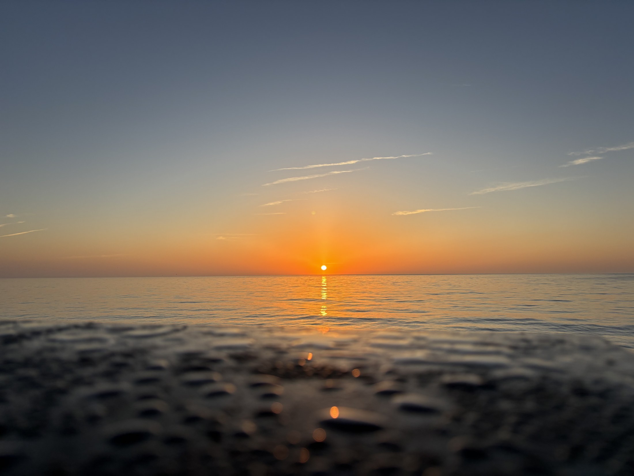 A low golden sun reflected in shallow pools across a broad wet shoreline